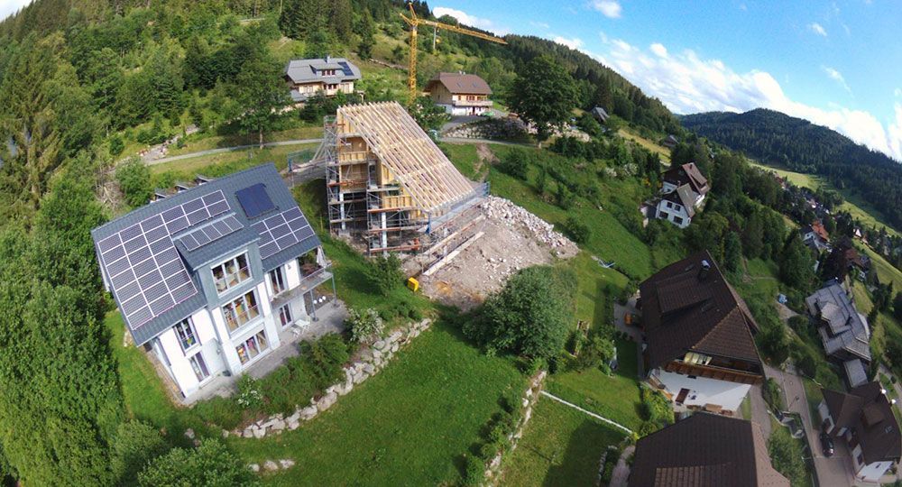 Luftaufnahme eines Hangviertels mit einem modernen Haus mit Solaranlage, einem im Bau befindlichen Gebäude und Bäumen.
