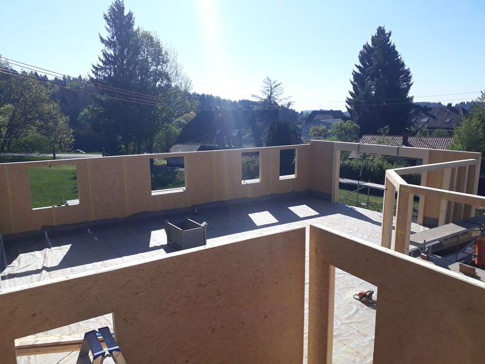 Eine Draufsicht auf eine Baustelle, die teilweise errichtete Außenwände aus OSB-Platten vor blauem Himmel zeigt.