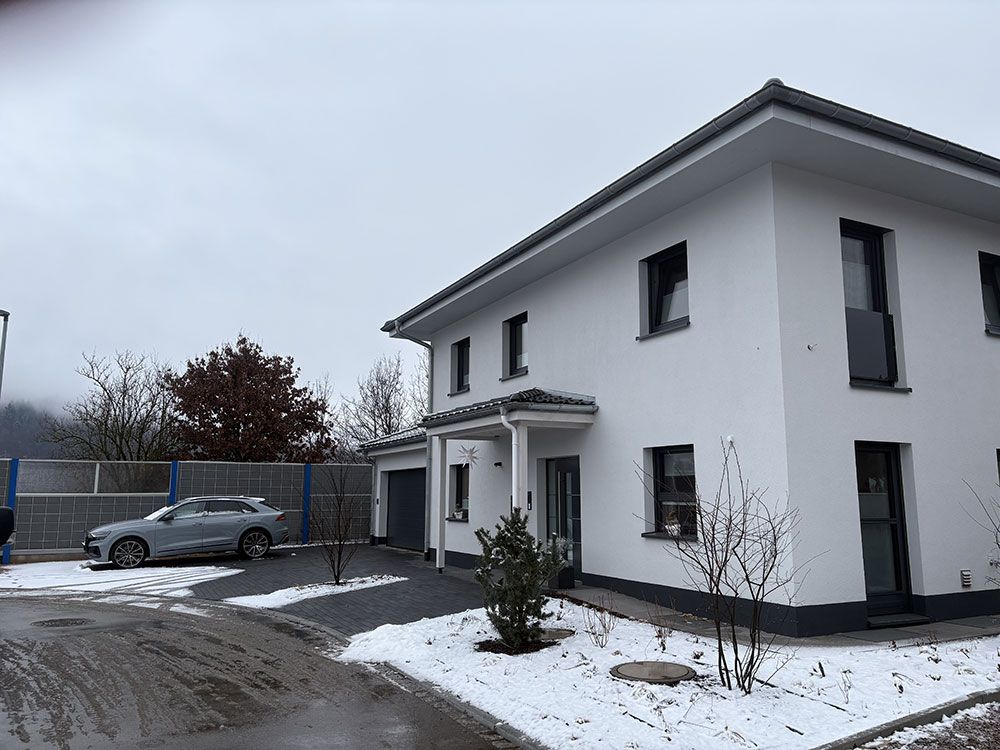 Ein weißes zweistöckiges Haus mit einem grauen Auto, das an einem verschneiten Wintertag in der Einfahrt parkt.