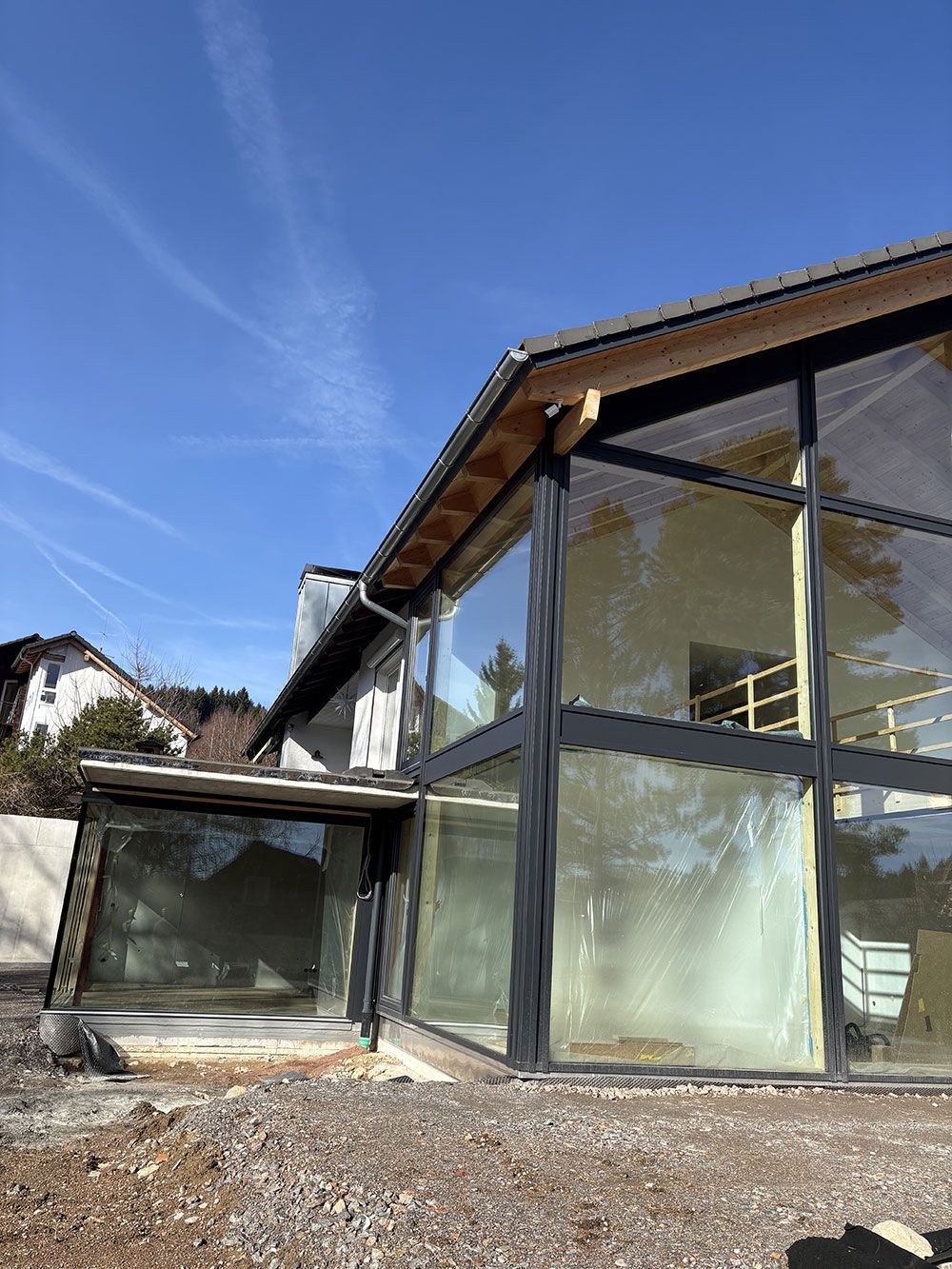 Ein modernes Gebäude mit großer Glasfassade und schwarzem Rahmen vor strahlend blauem Himmel.