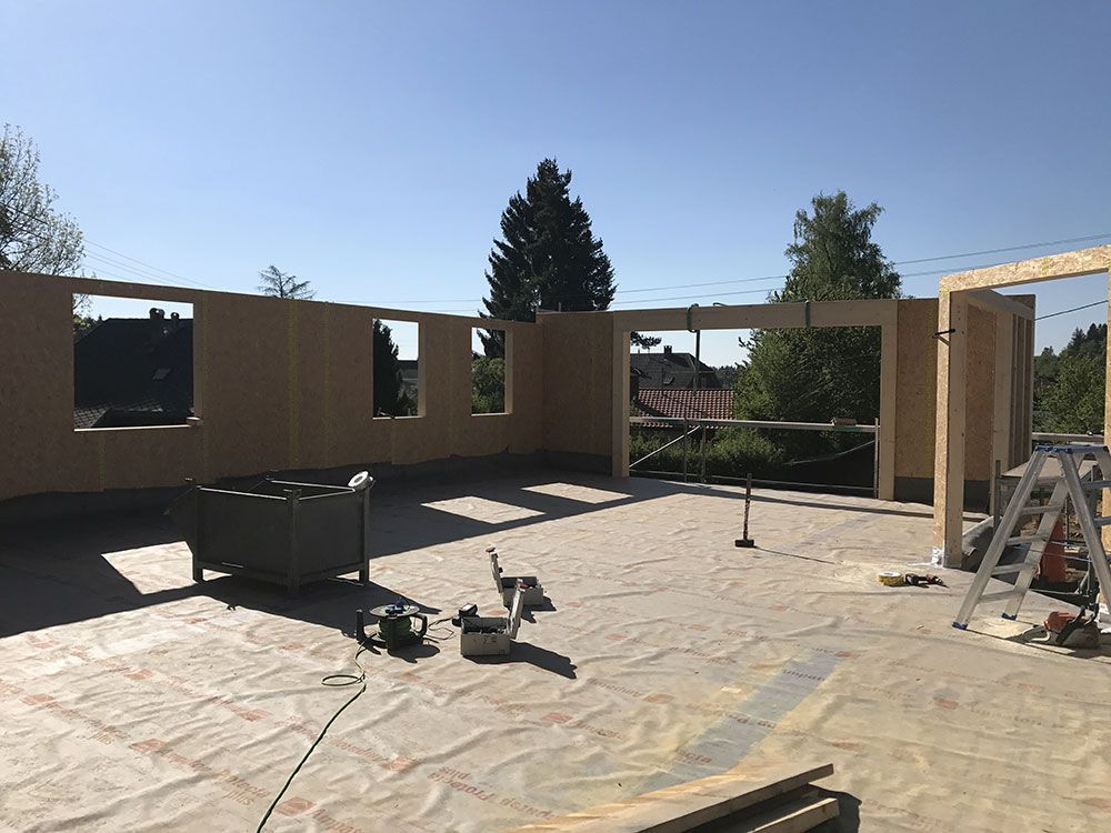 Baustelle mit Holzwandpaneelen, Fensteröffnungen und Werkzeugen auf einem mit Schutzmaterial bedeckten Boden.