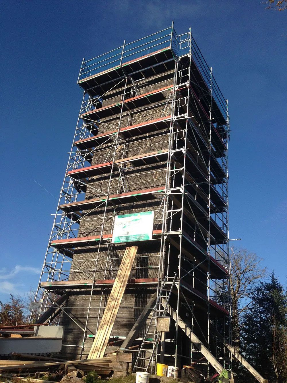 Ein Steinturm, der gerade renoviert wird und von einem hohen Metallgerüst umgeben ist, vor einem klaren blauen Himmel.