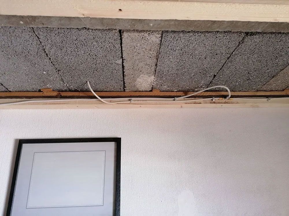 Unter einer unfertigen Decke mit freiliegenden Betonblöcken und Kabeln hängt ein gerahmtes Foto einer Personengruppe.