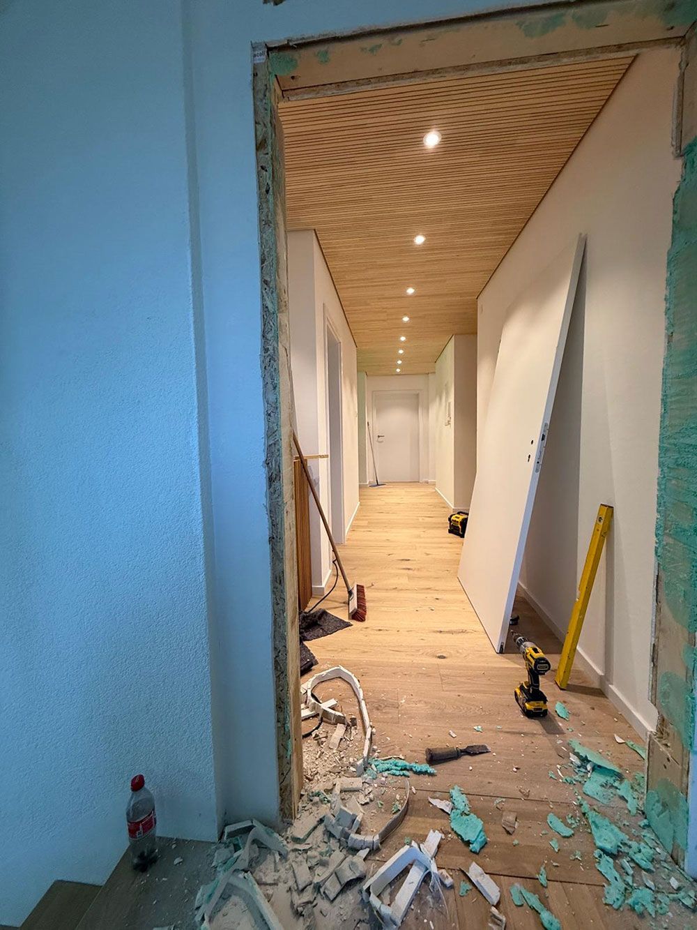 Ein im Bau befindlicher Flur mit einer gemusterten Holzdecke, Bauschutt auf dem Boden und einem schiefen Türrahmen.