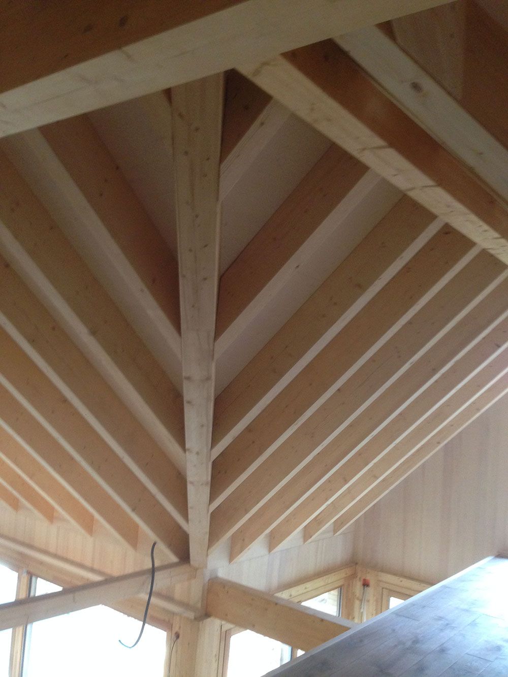 Eine Ansicht aus der Froschperspektive auf eine unfertige Holzdachkonstruktion, die Holzbalken zeigt, die an einem zentralen Firstbalken zusammenlaufen.