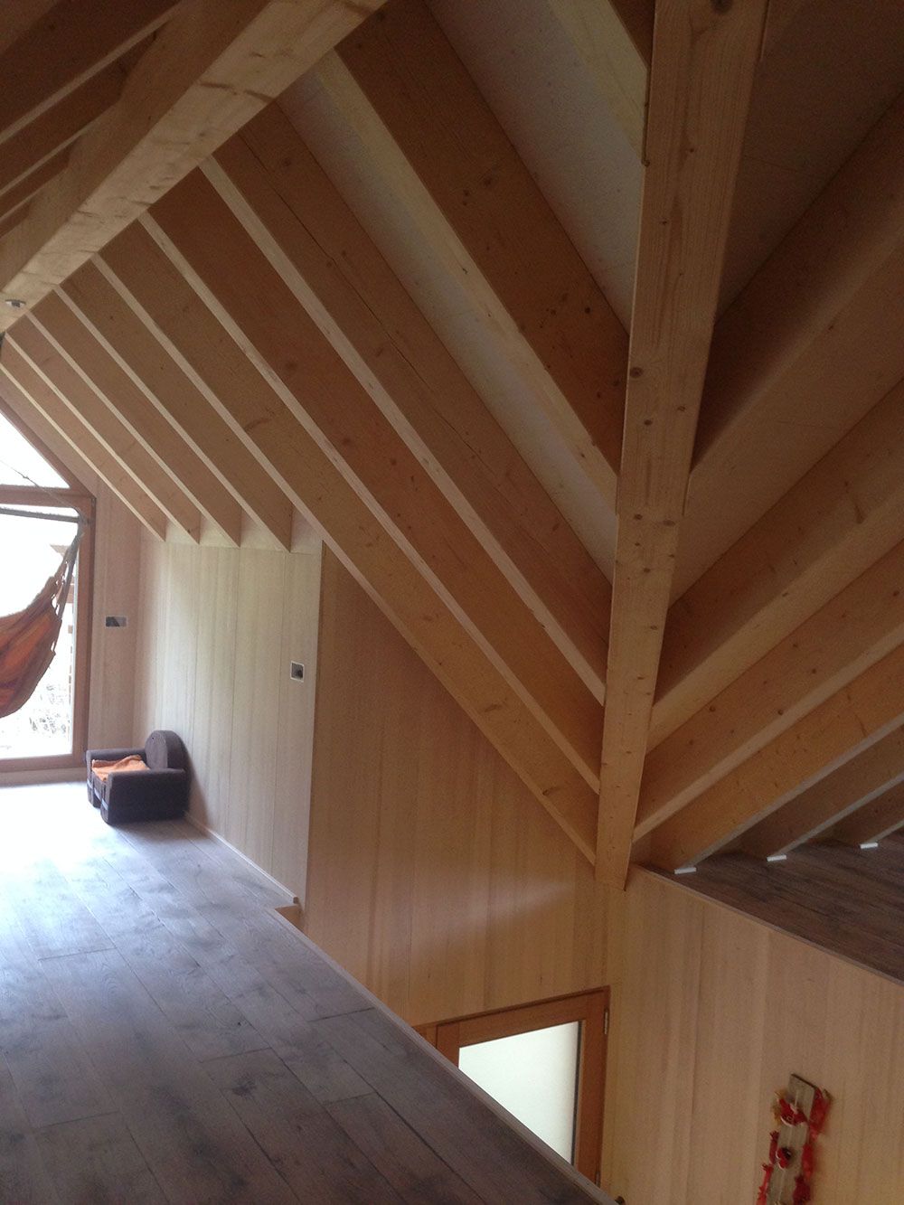 Innenansicht eines Dachbodens mit freiliegenden Holzbalken, hellen Holzwänden und einem Fußboden unter einer Gewölbedecke.