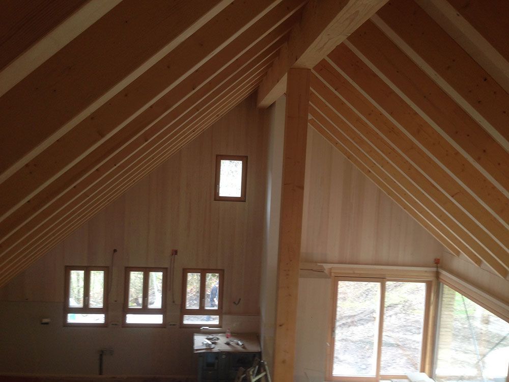 Ein geräumiges, unausgebautes Dachgeschoss mit freiliegenden Holzbalken, hellen holzgetäfelten Wänden und mehreren Fenstern.
