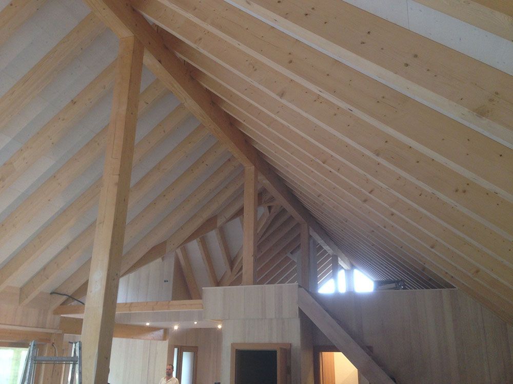 Innenansicht eines ausgebauten Dachbodens mit freiliegenden Holzbalken an der Decke und unbehandelter Holzvertäfelung an den Wänden.