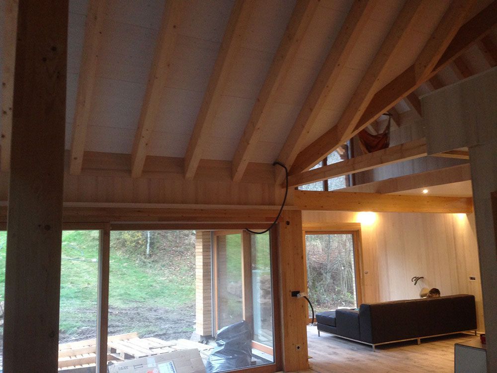 Innenansicht eines modernen Holzhauses mit gewölbten Decken, großen Fenstern mit Blick auf einen Hof und einem Wohnbereich.