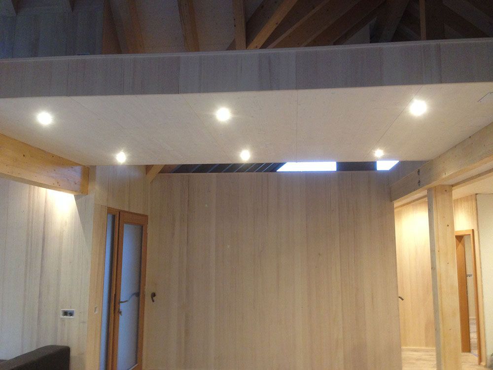 Ein modernes Interieur mit hellen Holzvertäfelungen, einem eingelassenen Deckenabschnitt mit sechs Strahlern und sichtbaren Holzbalken.
