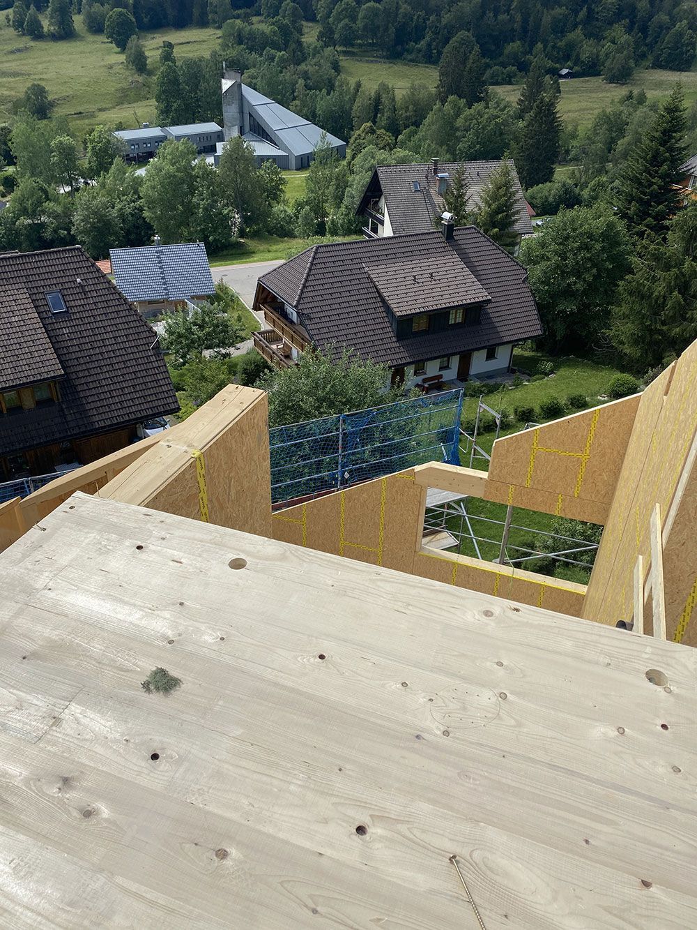 Blick aus der Vogelperspektive auf ein im Bau befindliches Holzgebäude mit Blick auf Häuser und ein grünes Tal.