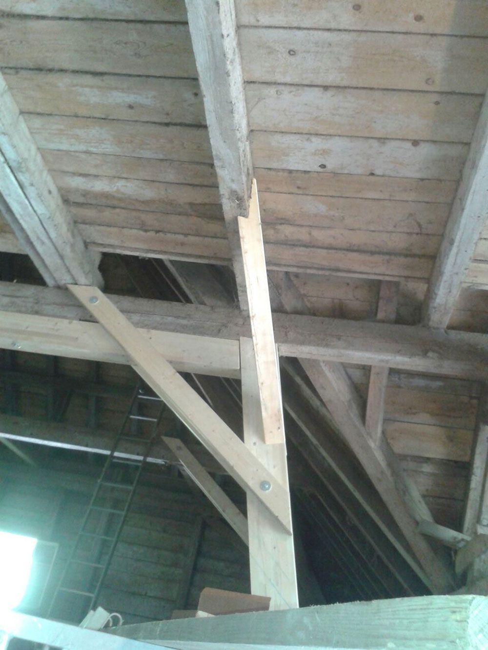Innenansicht der hölzernen Dachsparren und Deckenbretter, auf der eine neue Holzreparaturstrebe an einem tragenden Pfosten zu sehen ist.