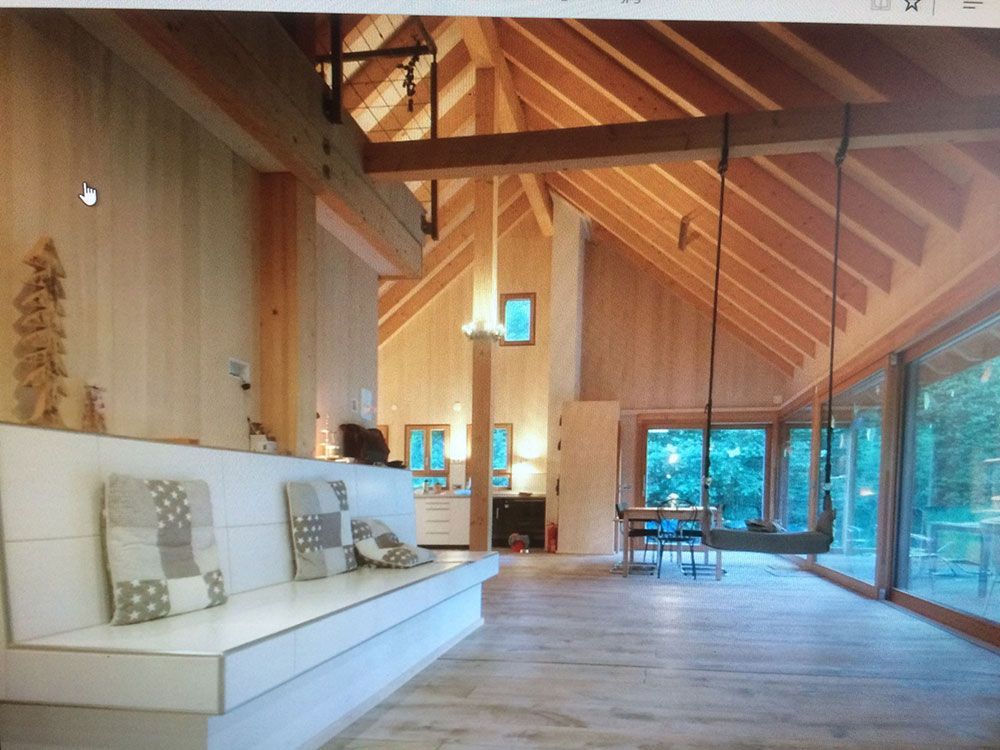 Ein moderner, offener Wohnbereich mit gewölbten Holzdecken, einer langen, weißen Einbaubank und einer Hängeschaukel für den Innenbereich.