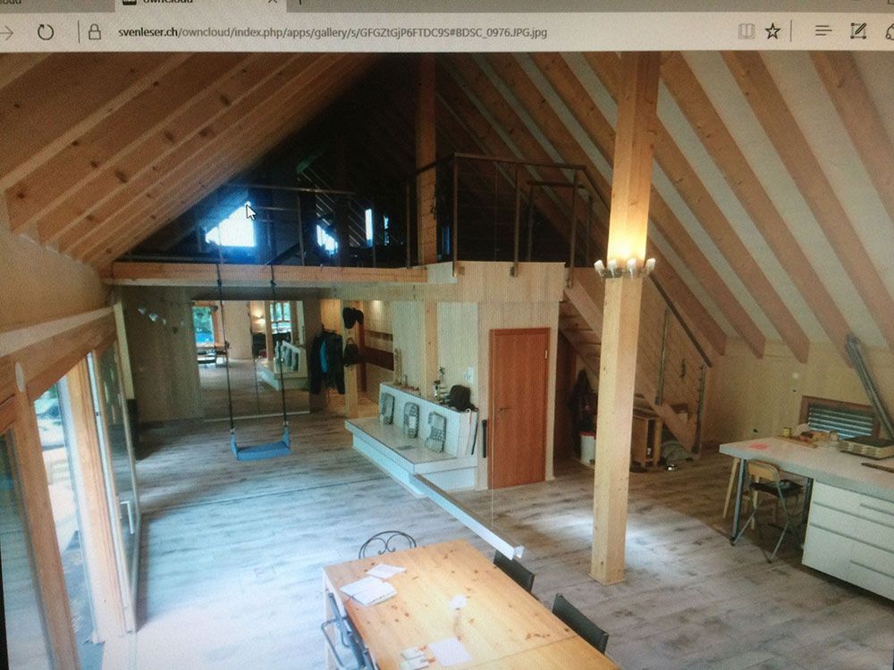 Ein offener Raum im rustikalen Stil mit hoher Holzbalkendecke, Esstisch, Galerie und hellem Fußboden.