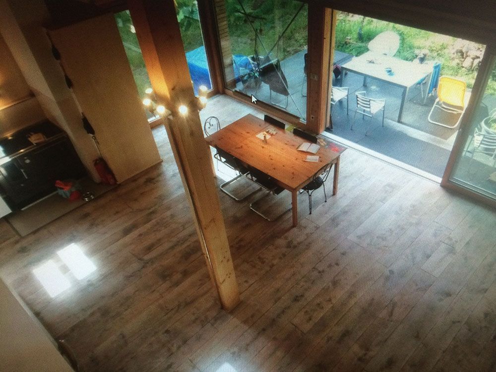 Draufsicht auf ein Esszimmer mit Holztisch, Stühlen und großen Glastüren, die sich zu einer Terrasse öffnen.