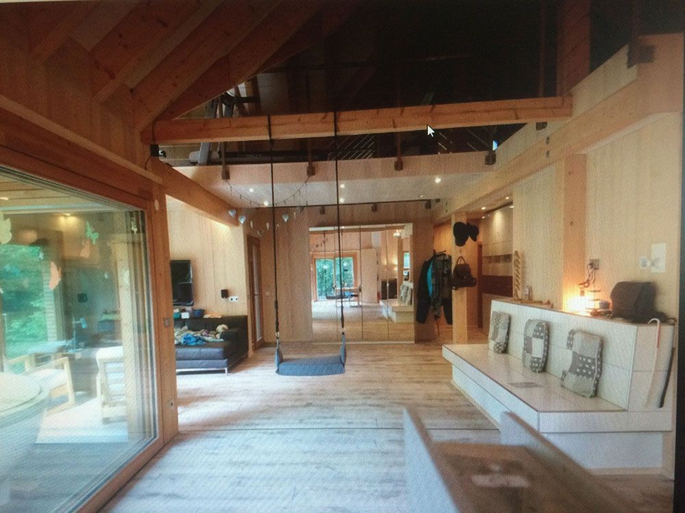 Ein modernes, holzgetäfeltes Zimmer mit hohen Dachbalken, einer zentralen Schaukel, einer eingebauten weißen Bank und großen Glasfenstern.