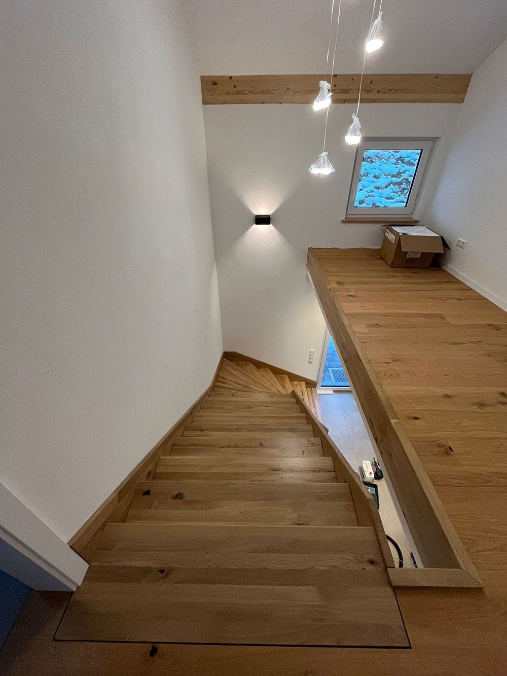 Blick von oben auf eine Holztreppe, die zu einem Treppenabsatz mit Holzboden, Oberlicht und wandmontierter Akzentbeleuchtung führt.