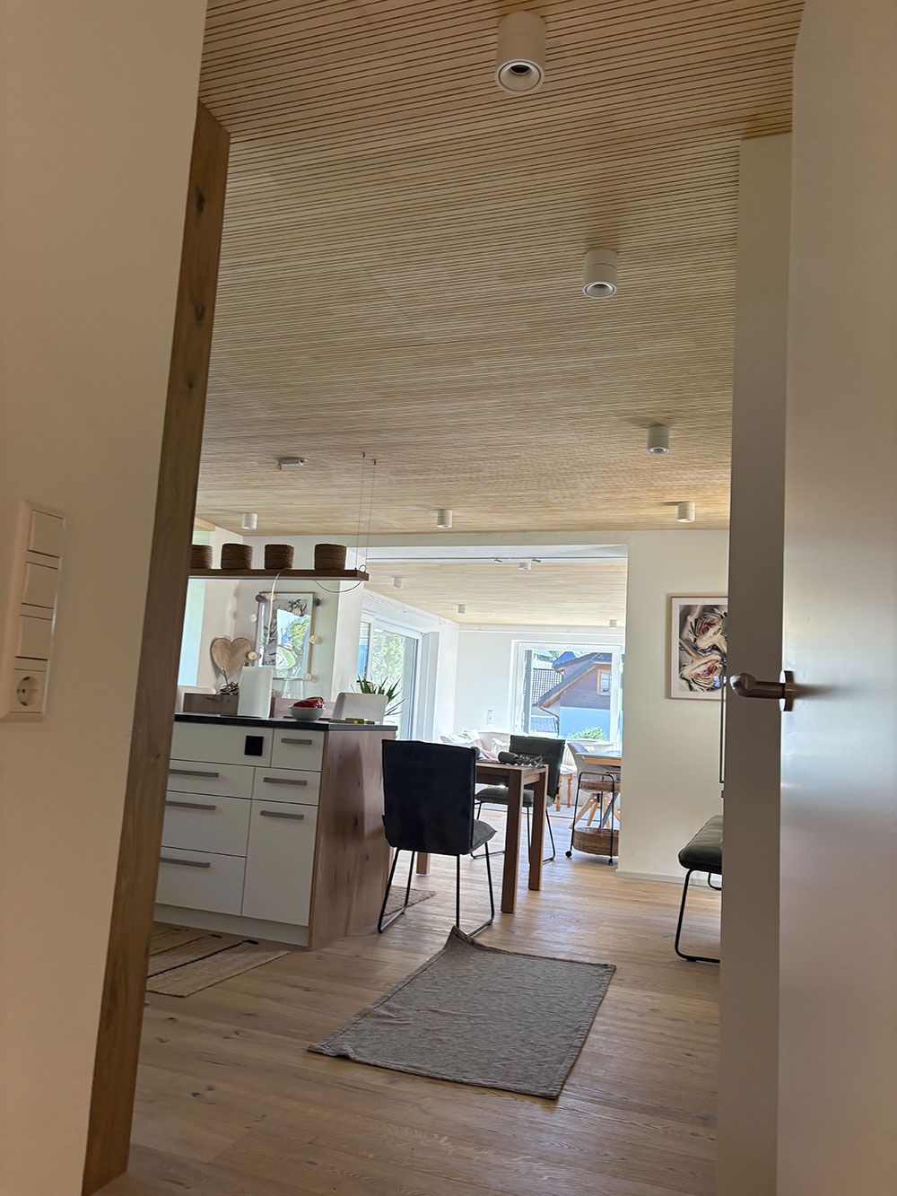 Ein Blick durch eine Türöffnung in ein Wohnhaus mit einer strukturierten, gemusterten Decke, einer Kücheninsel und einem Essbereich.