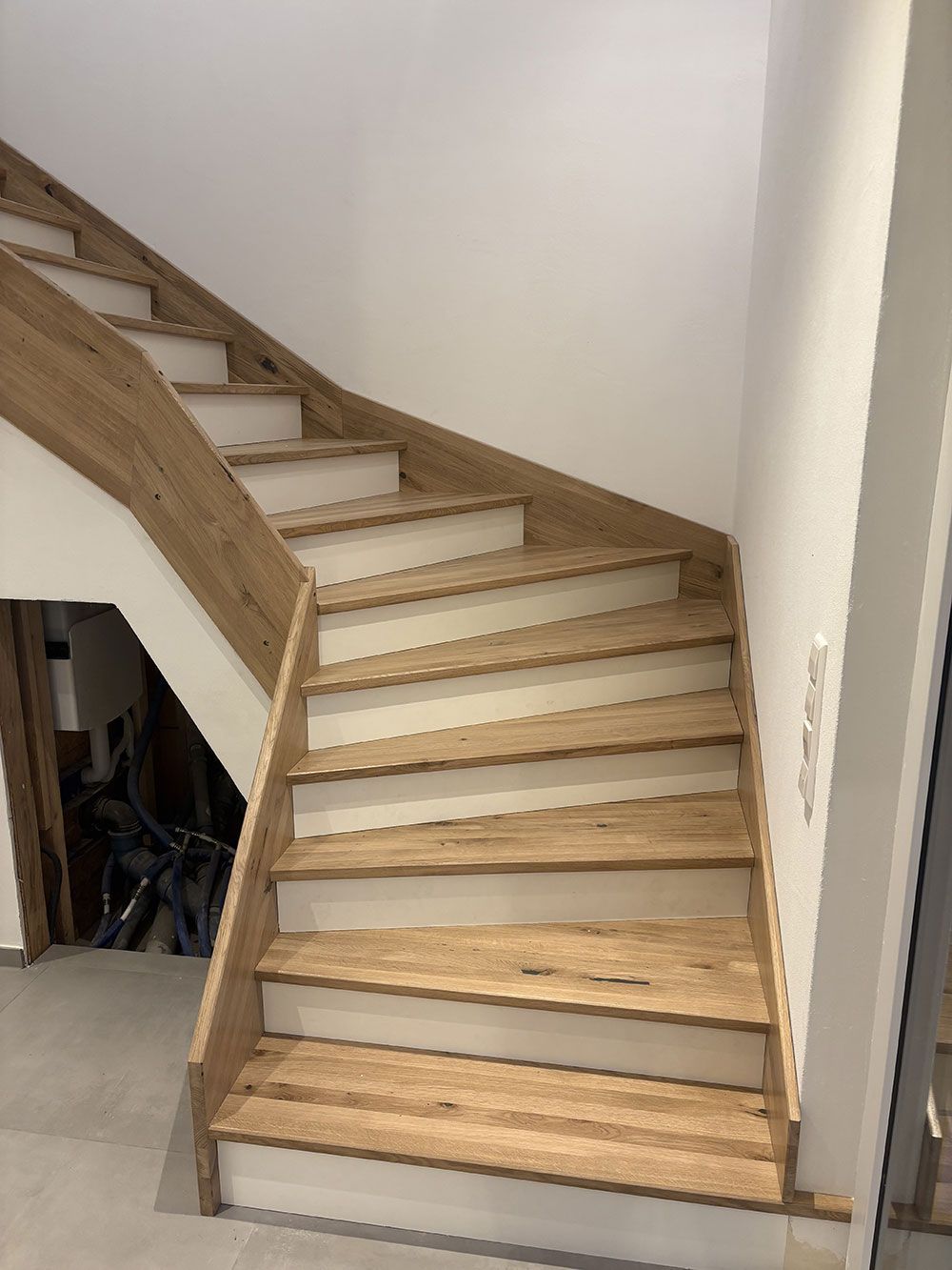 Eine Treppe mit hellen Holzstufen und weißen Setzstufen, die sich in einem modernen Interieur zwischen zwei weißen Wänden nach oben windet.