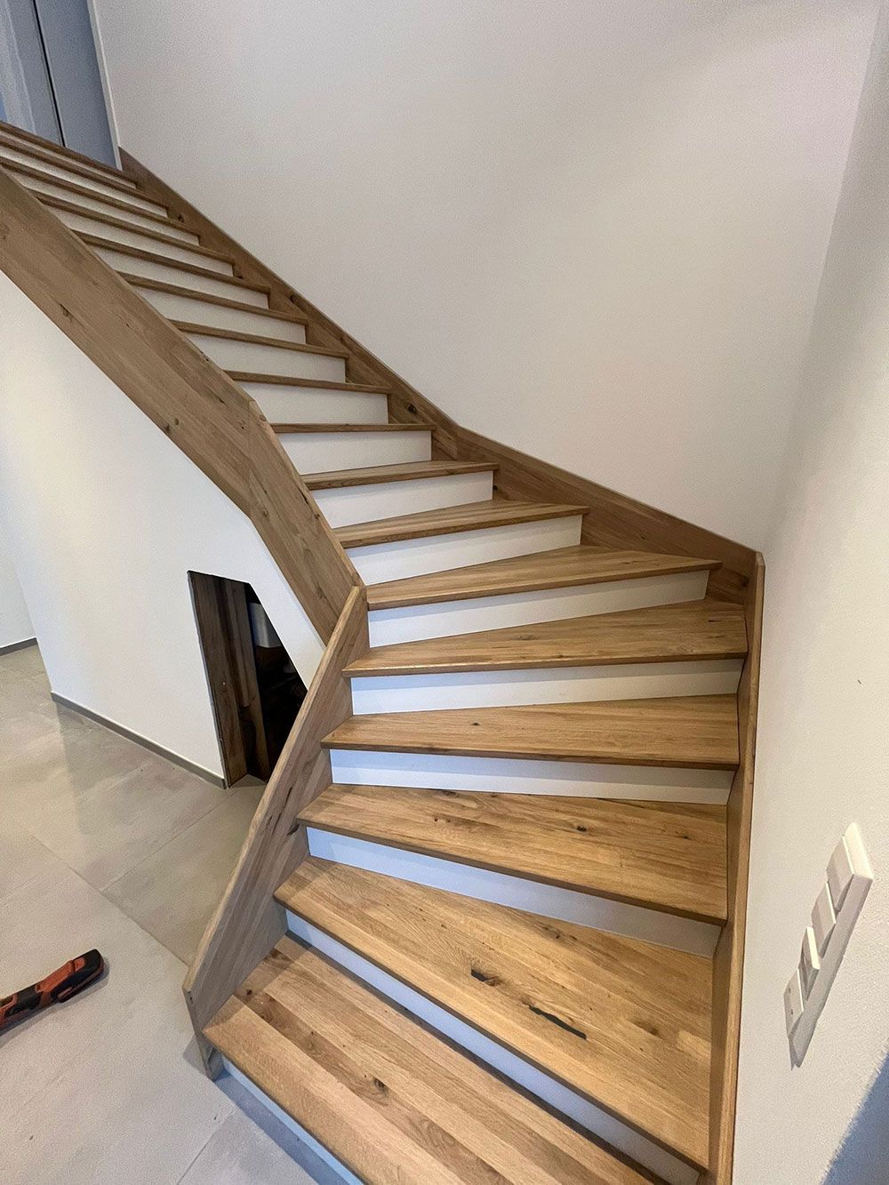 Eine hölzerne Treppe mit weißen Setzstufen, die sich in einem hellen Raum mit hellen Böden und Wänden nach oben windet.