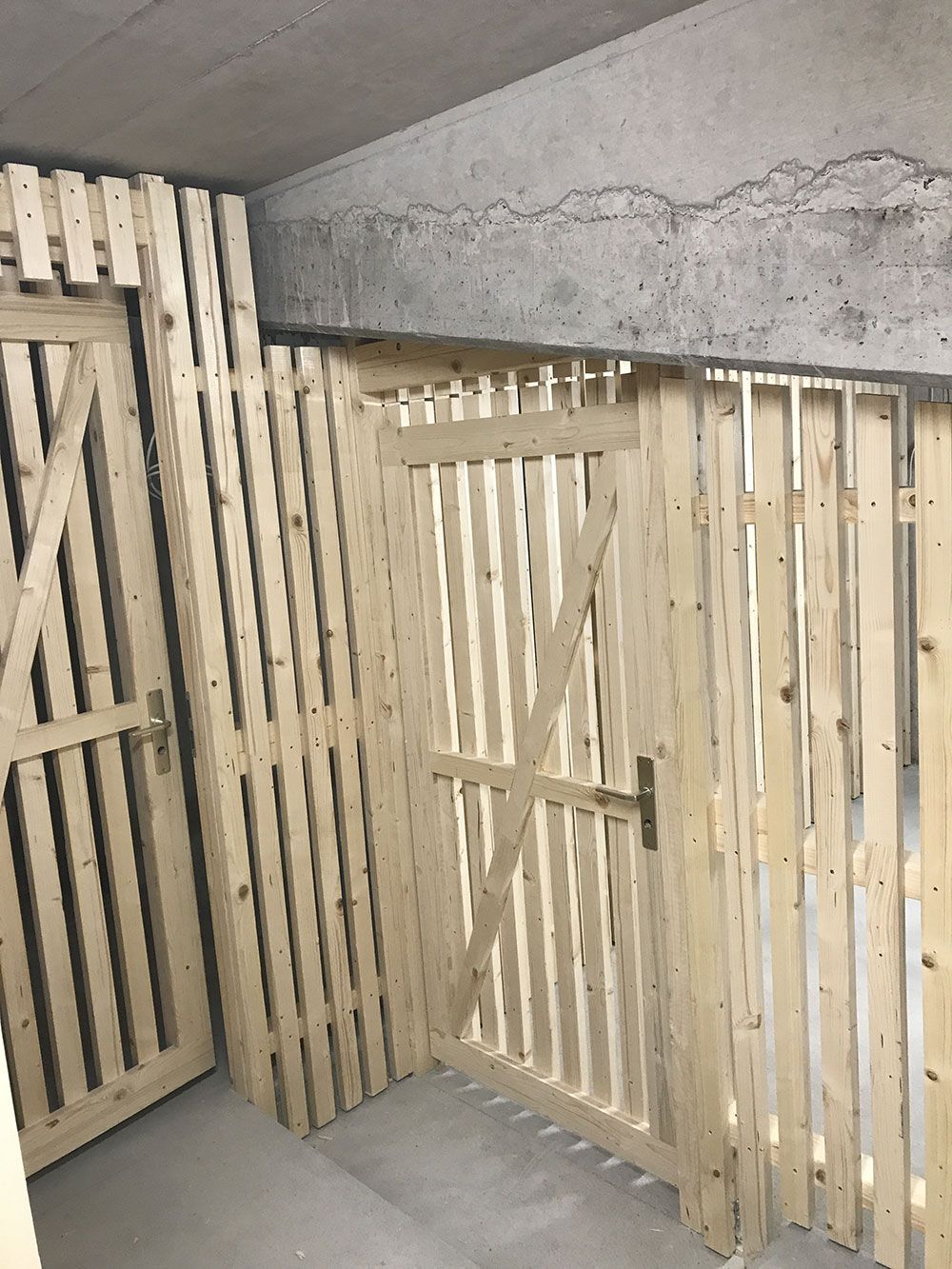 Helle, mit Holzlatten verkleidete Aufbewahrungsschränke mit Türen, die an einer Betonwand in einem Lagerraum oder Keller installiert sind.