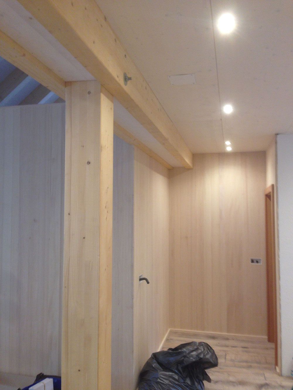 Innenansicht eines Flurs mit hellen Holzvertäfelungen an den Wänden, sichtbaren Holzbalken an der Decke und Einbauleuchten.