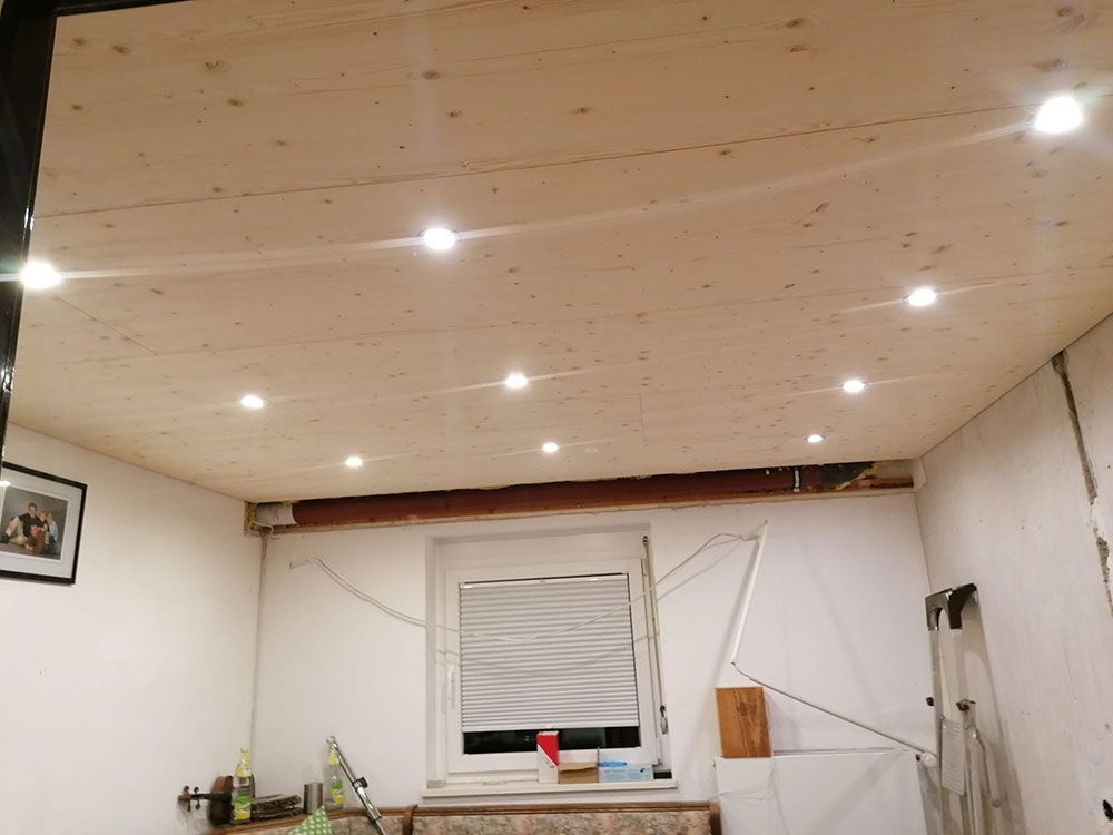 Ein Zimmer mit einer neu installierten, hellen Holzpaneeldecke und mehreren eingelassenen LED-Spots über weißen Wänden.
