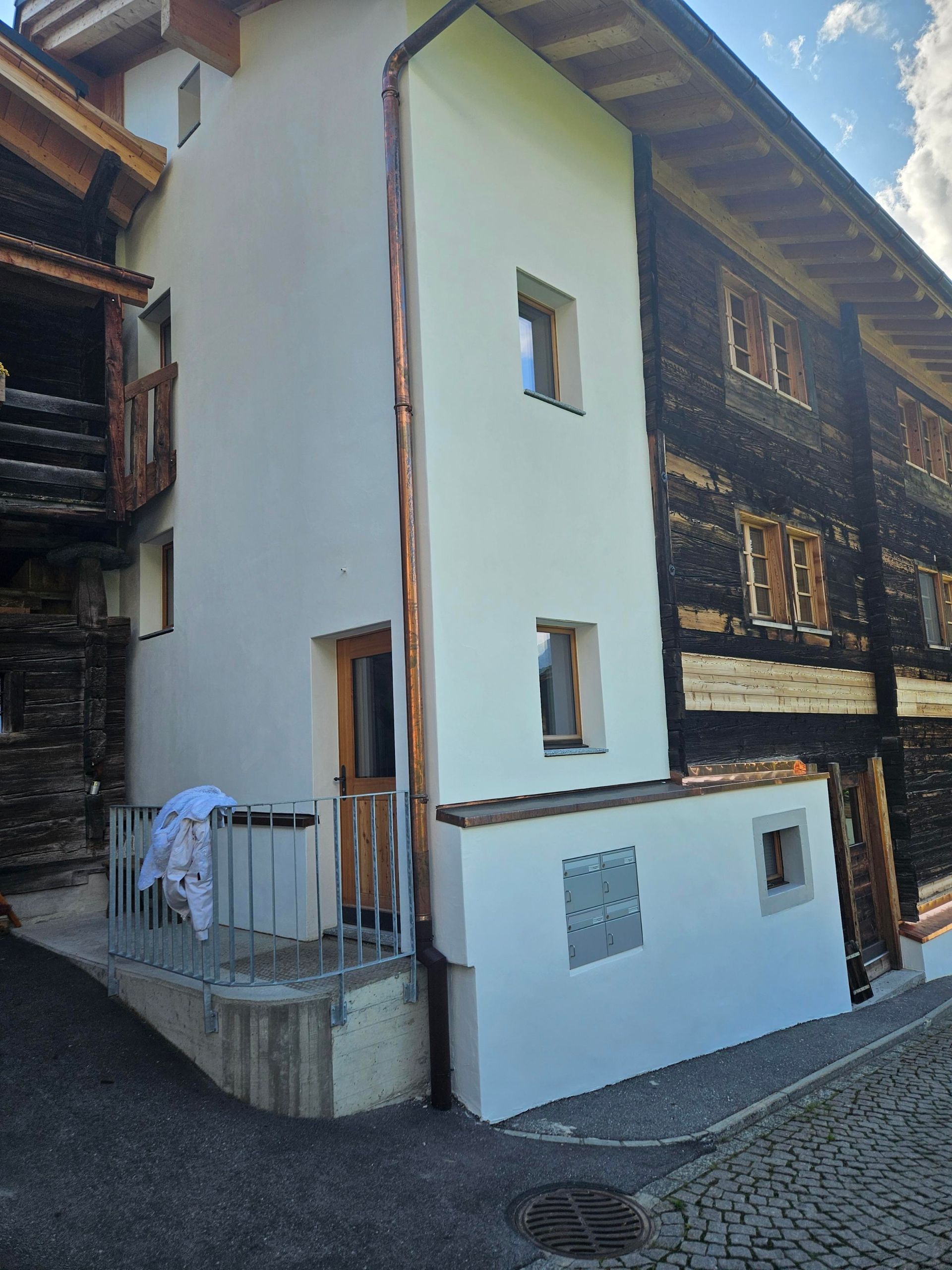 Maler in Overall und Schutzhelm streicht mit einer Rolle eine weiße Wand in einem unfertigen Raum.