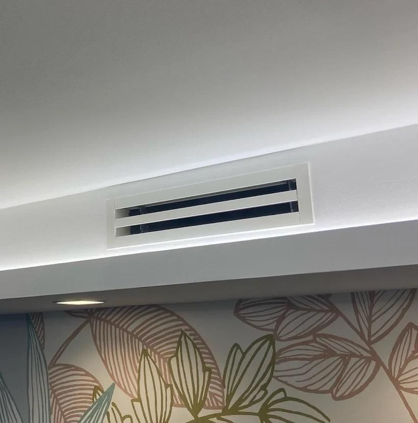 Grille d'aération dans un plafond blanc, avec un mur décoratif en dessous.