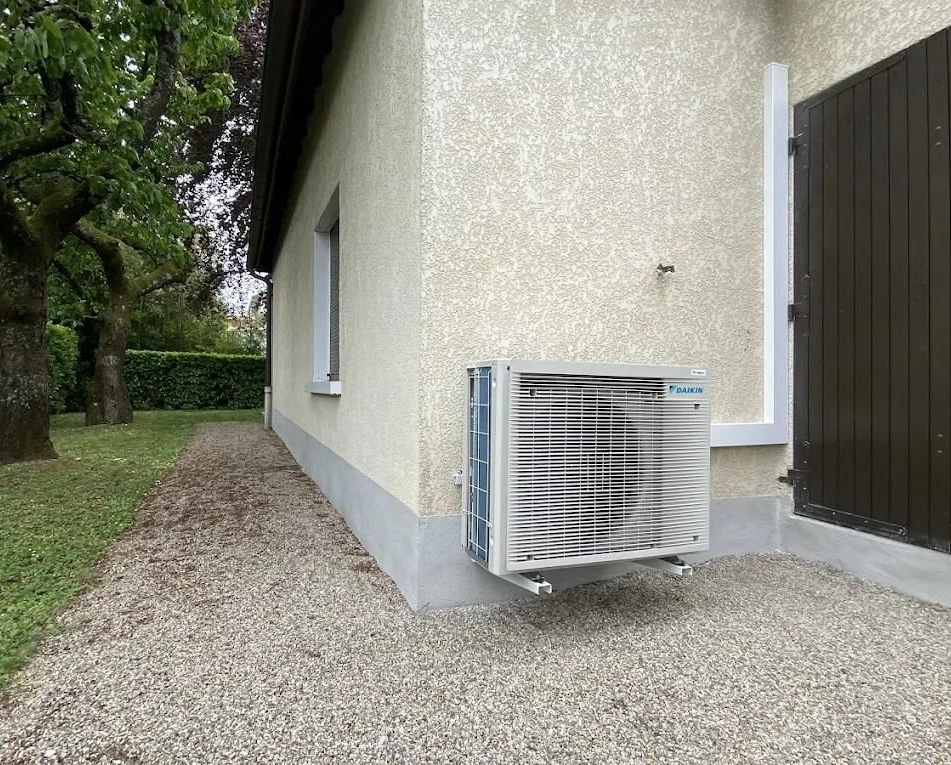 Un climatiseur monté sur le mur extérieur d'un bâtiment dont le sol est recouvert de gravier.
