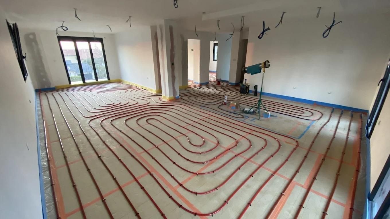 Installation d'un système de chauffage au sol dans une pièce. Tuyaux rouges posés sur l'isolant, prêts pour la pose du revêtement de sol. Câbles pendant du plafond.