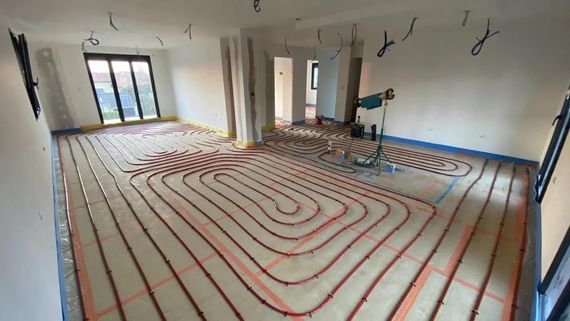 Installation d'un système de chauffage au sol dans une pièce. Tuyaux rouges posés sur l'isolant, prêts pour la pose du revêtement de sol. Câbles pendant du plafond.