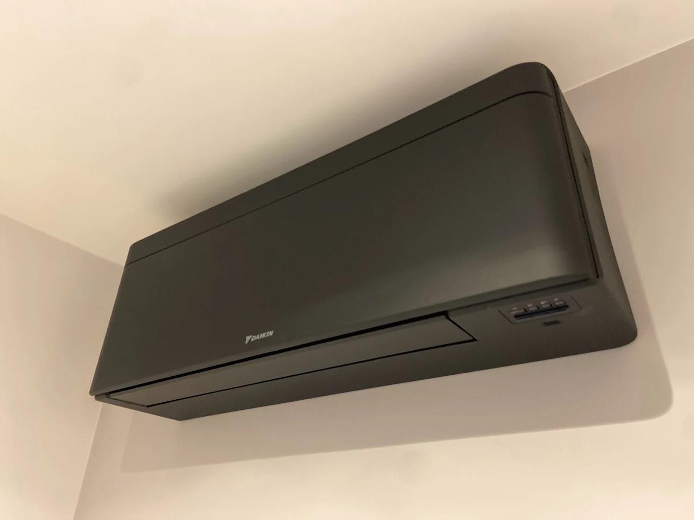 Climatiseur Daikin gris foncé, fixé sur un mur blanc dans un coin.