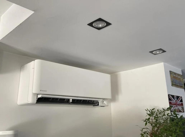 Unité de climatisation blanche fixée sur un mur blanc ; plafond avec spots encastrés.