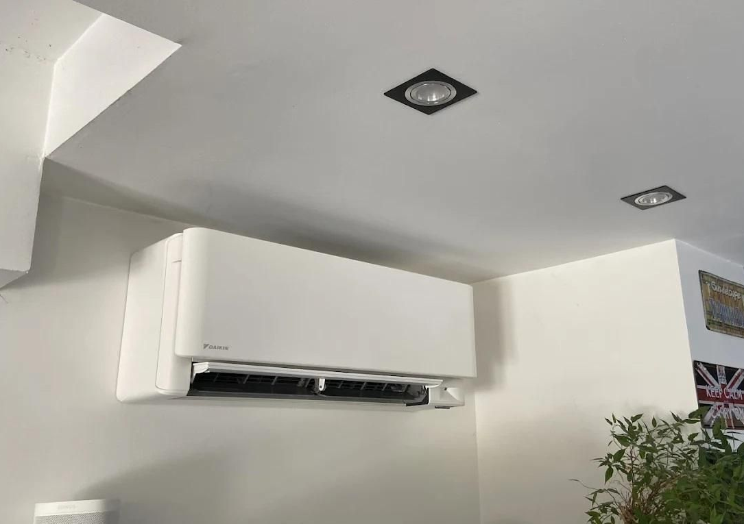 Unité de climatisation blanche fixée sur un mur blanc dans une pièce avec éclairage encastré.
