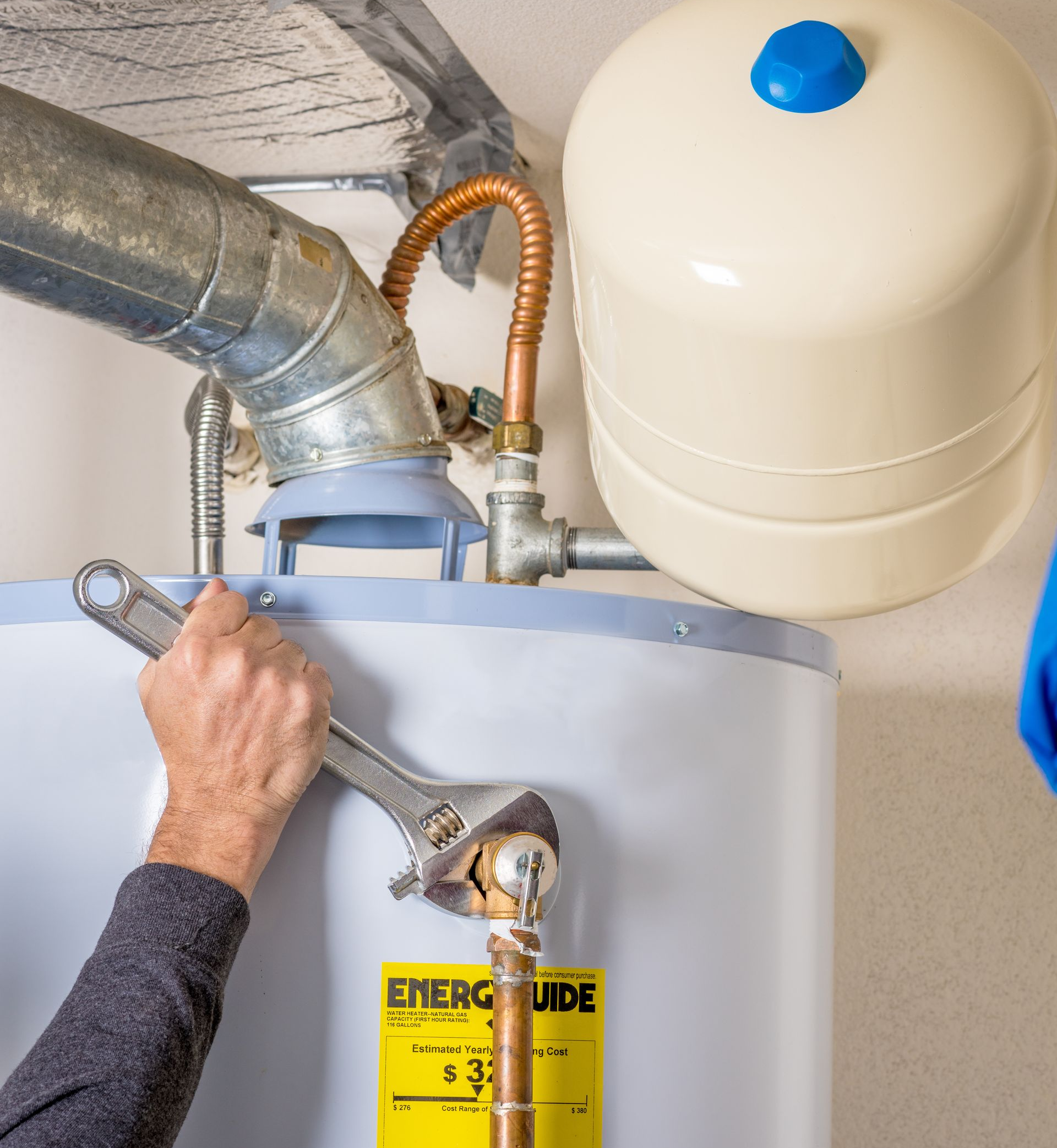 Une personne utilise une clé sur un chauffe-eau, avec un vase d'expansion à proximité.