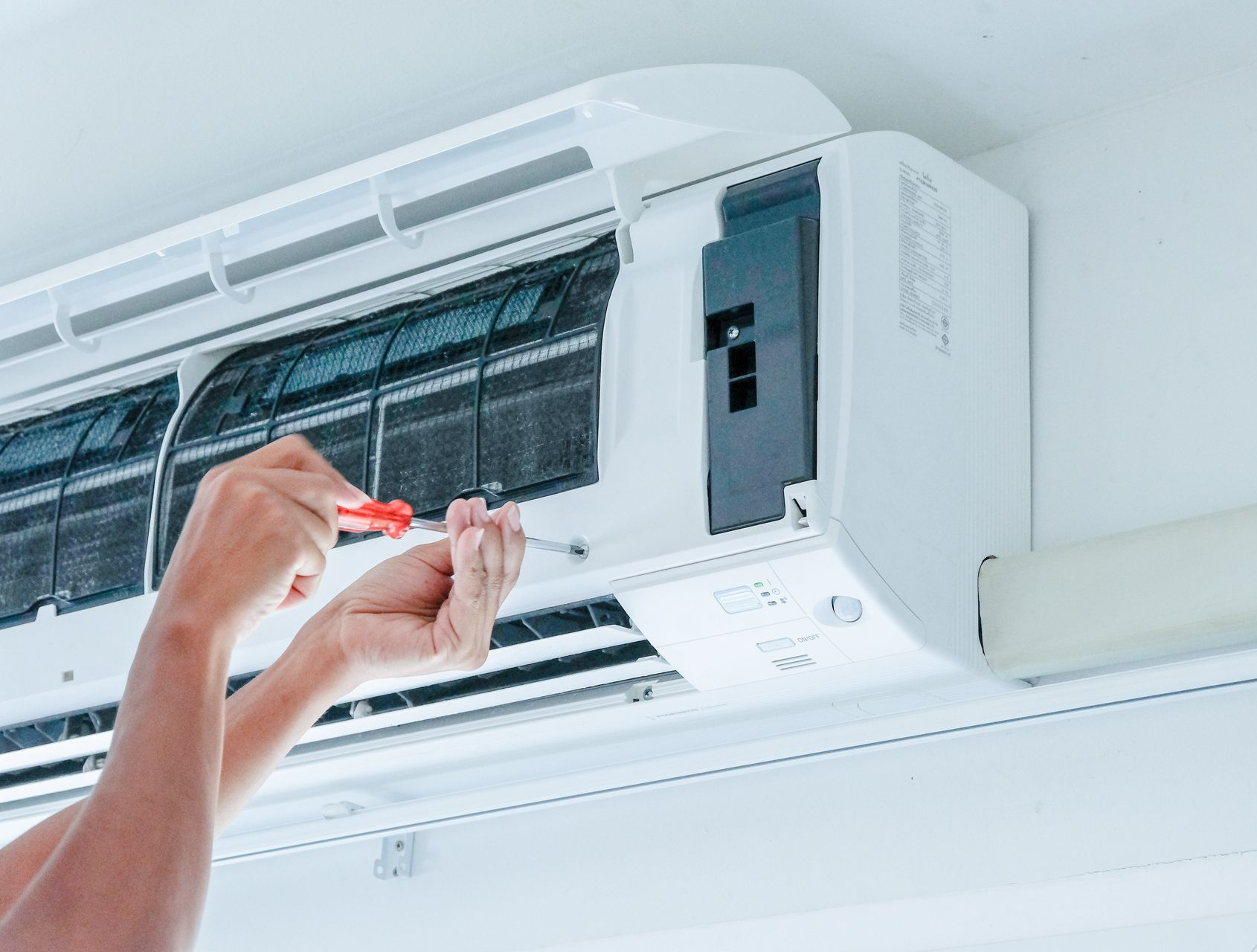 Une personne utilise un tournevis pour réparer un climatiseur mural blanc.
