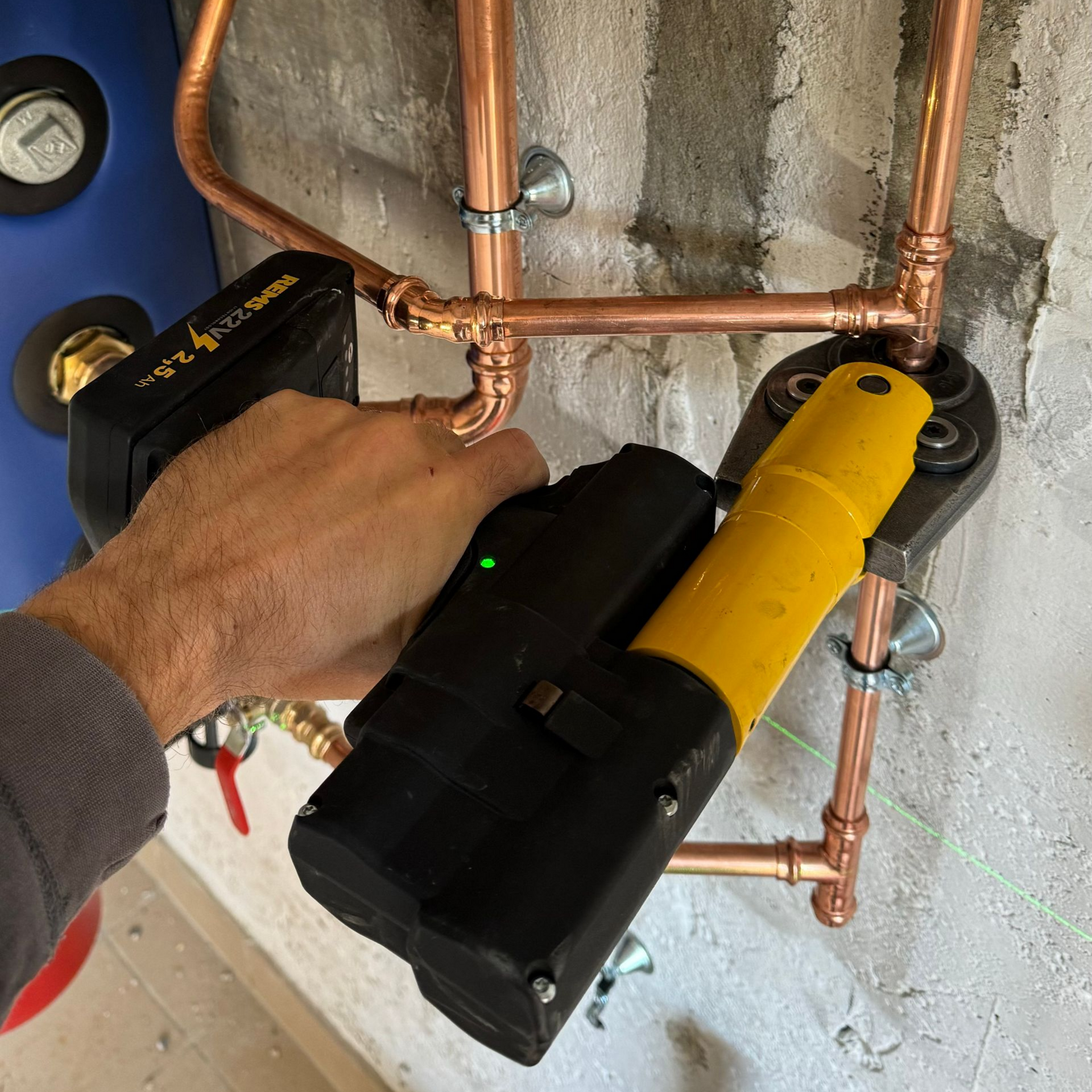 Chauffe-eau bleu et noir avec tuyaux en cuivre sur un mur blanc.