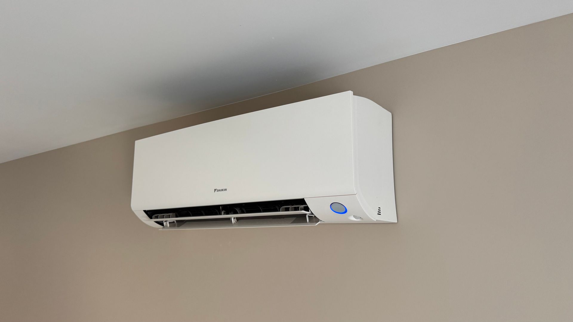 Climatiseur mural blanc sur un mur beige, sous un plafond blanc.