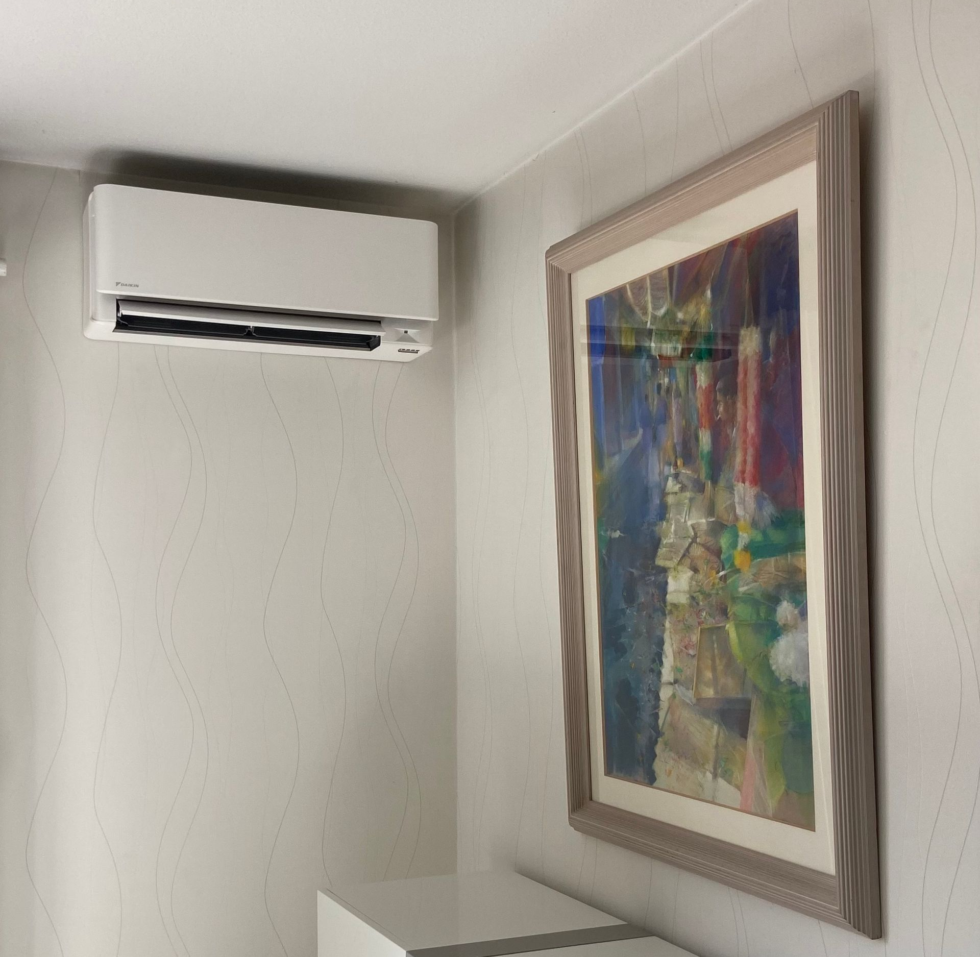 Unité de climatisation blanche fixée sur un mur blanc au-dessus d'une télévision et de meubles bleus.