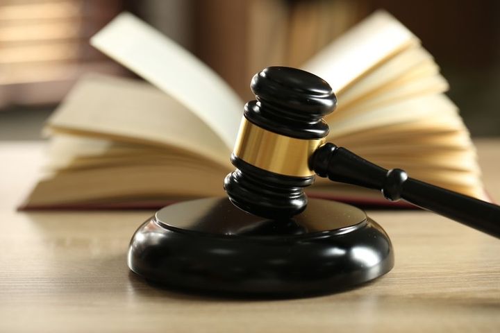 Mazo sobre un bloque de madera, delante de un libro de leyes abierto, en interiores, primer plano.