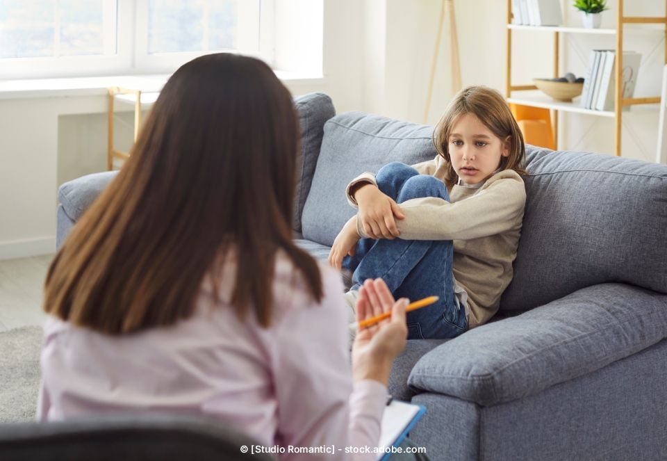 Ein Kind sitzt mit seinem Therapeuten auf einem Sofa und sieht besorgt aus.