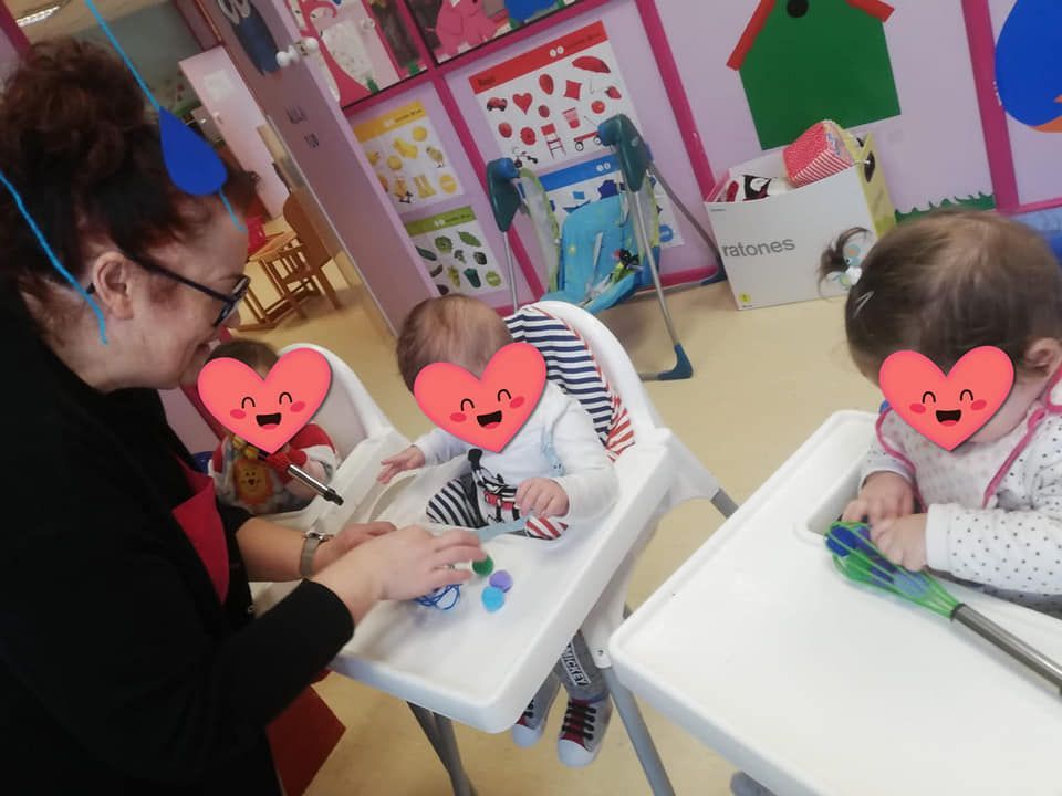 Una mujer está jugando con tres bebés en sillas altas.
