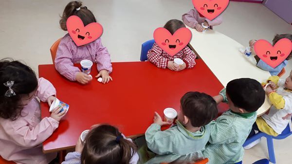 Un grupo de niños están sentados en una mesa con corazones en sus caras.