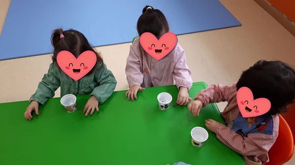 Tres niños con corazones en sus caras están sentados en una mesa con tazas.