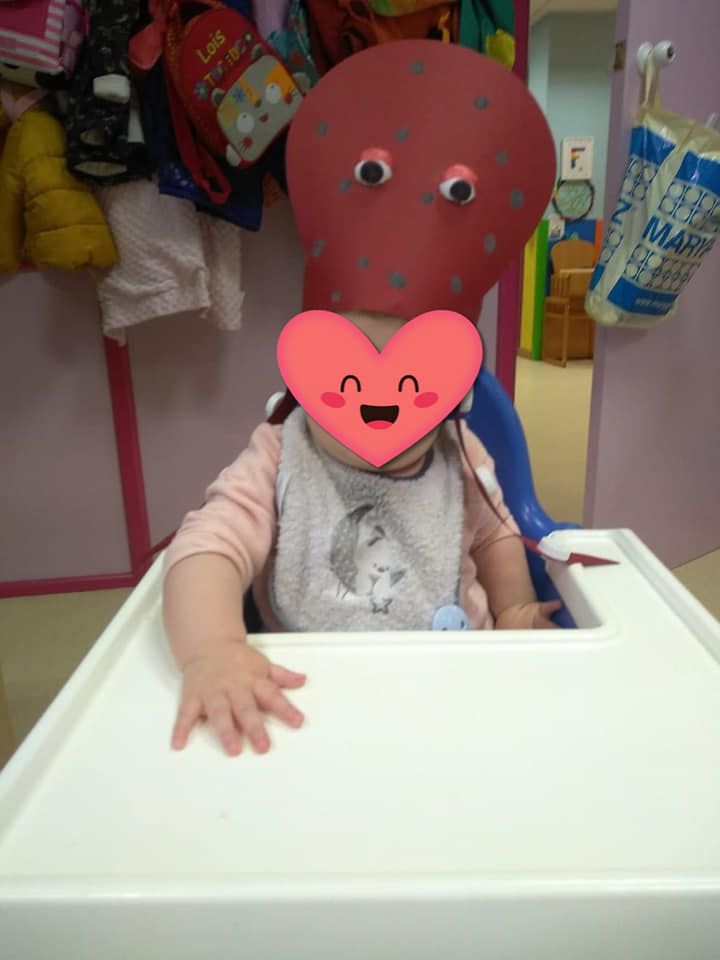 Un bebé con una máscara de pulpo rojo está sentado en una silla alta.