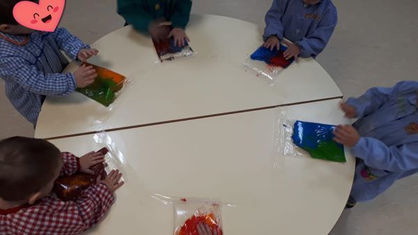 Un grupo de niños están sentados alrededor de una mesa jugando con bolsas de gelatina.