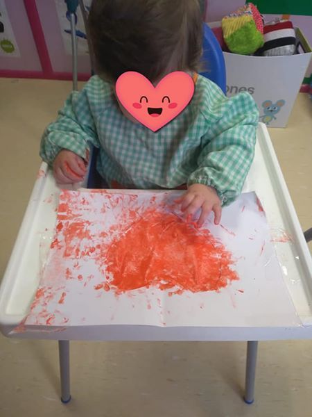 Una niña está sentada en una silla alta con un corazón rosa en la cara.