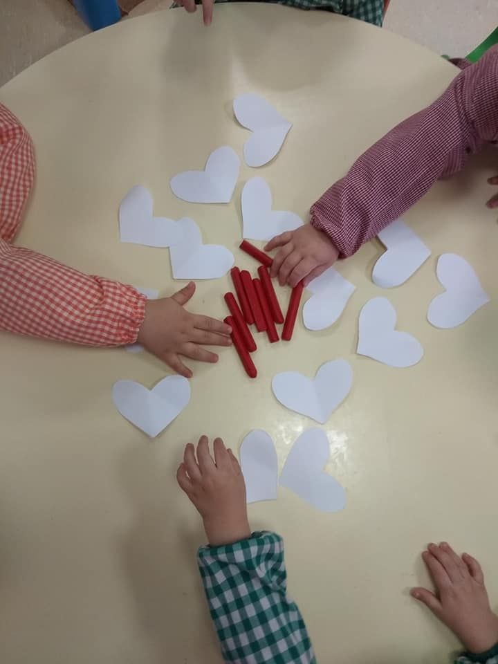 Los niños están jugando con corazones de papel y palitos rojos sobre una mesa.