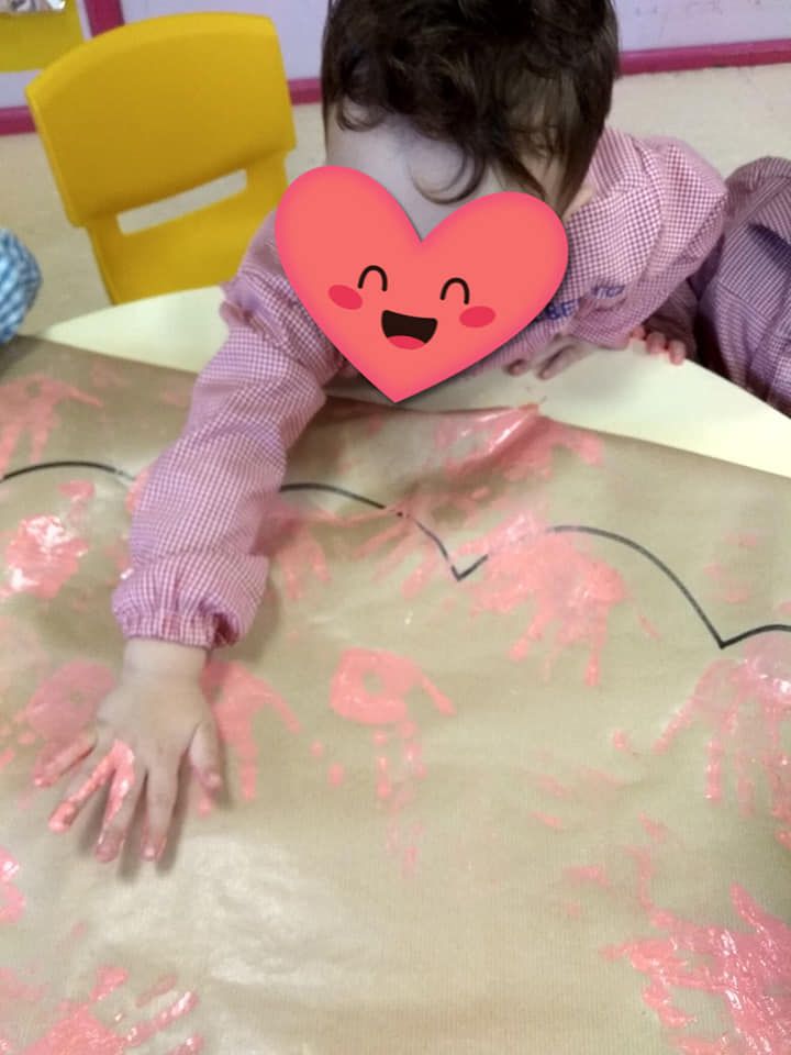 Una niña con un corazón en la cara está jugando con pintura rosa.